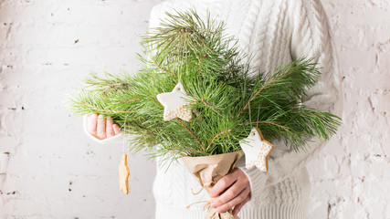 Female hands holding a Christmas bouquet of branches of spruce decorated with a pastry star. New year. Settle background , kinfolk