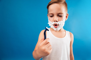 Surprised young boy in shaving foam looking at razor