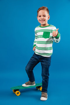Full length image of pleased young boy posing with skateboard