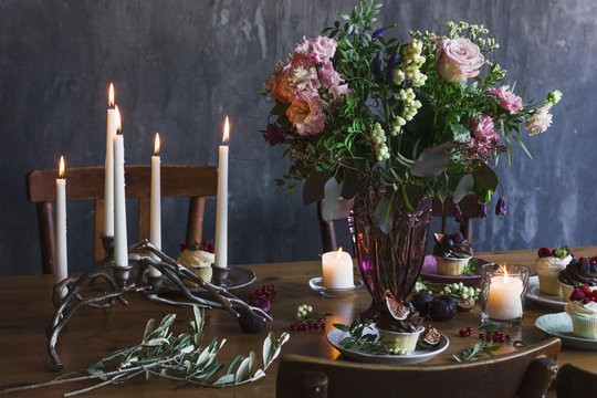 Festive table with bouquet of flowers, candles and cupcakes