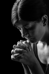 Faithful woman praying, hands folded in worship to god with head down and eyes closed in religious fervor, on a black background. Concept for religion, faith, prayer and spirituality.
