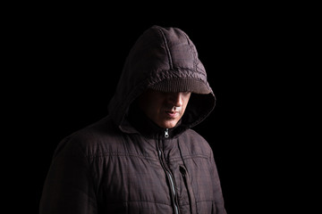 Fototapeta na wymiar Scary and creepy man hiding in the shadows, with the face and identity hidden with the hood, and standing in the darkness. Low key, black background. Concept for fear, mystery, danger, crime, stalker
