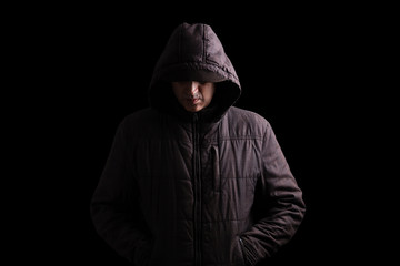 Fototapeta na wymiar Scary and creepy man hiding in the shadows, with the face and identity hidden with the hood, and standing in the darkness. Low key, black background. Concept for fear, mystery, danger, crime, stalker