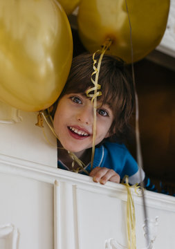 Little boy looking at camera holding balloons while laying in the wardrobe