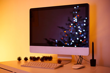 Christmas workspace interior with decorated christmas tree reflection in monitor and pine cones on...