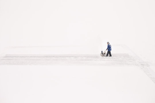 Man pushing snow blower on lake to prepare an ice rink