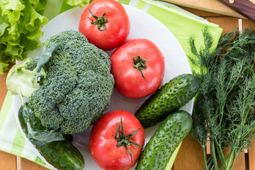 Fresh raw vegetables on white plate on wooden table, top view.