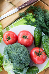 Fresh raw vegetables on white plate on wooden table, top view.