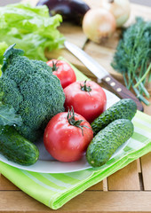 Fresh raw vegetables on white plate on wooden table, vertical view