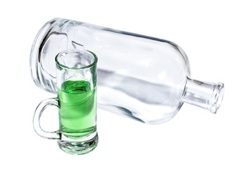 Empty transparent bottle and a glass filled with a green absinthe.