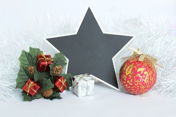 Une ardoise vide en forme d'étoile pour écrire un message avec des cadeaux rouges et blancs, des feuilles vertes,une couronne de sapin et une boule rouge ,une guirlande blanche brillante givrée sur un