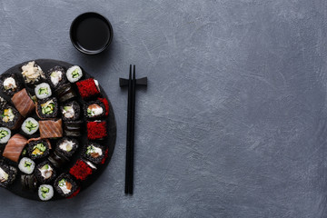 Set of black sushi rolls, maki with chopsticks on gray background, top view