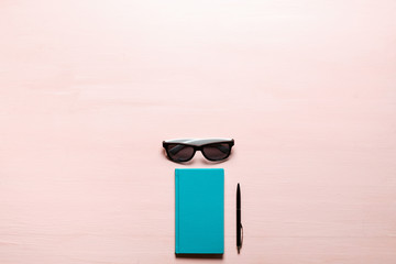 Fototapeta na wymiar Aquamarine diary, black pen, sunglasses on pink textplace background. flat lay, top view.