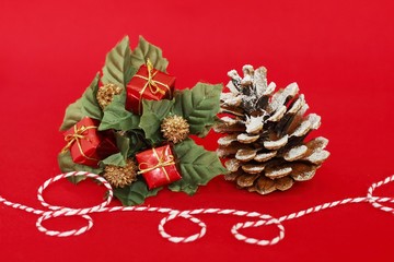 Des cadeaux rouges, des feuilles vertes et une pomme de pin ainsi q'un fil rouge et blanc pour décorer les fêtes sur un fond rouge