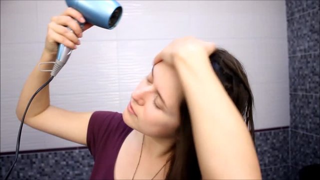 Happy young woman blow drying hair in bathroom