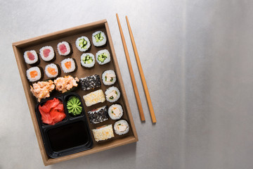 Top view set of sushi maki and rolls with chopstics, rice, soy, wasabi and ginger on grey background