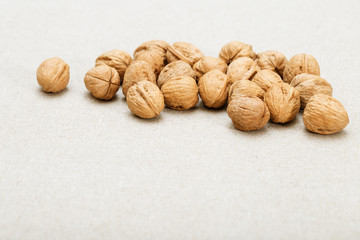 Bunch of round whole walnuts on a very light blurred fabric background.