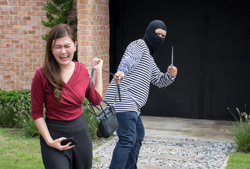 Male robber robbing a handbag threatening with knife to scared Asian woman,criminal concept