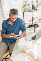Obraz na płótnie Canvas Sitting at his desk an architect using a digital tablet