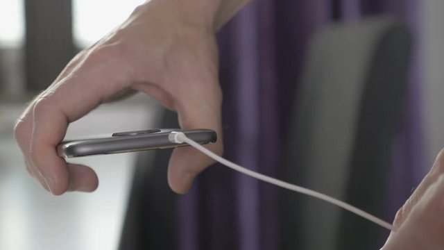 Man plugging in wire to headphone jack on a smartphone