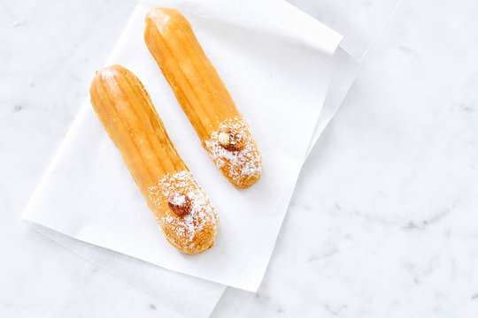 Two eclairs with caramel cream on white marble background