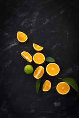 oranges, lime, lemon with green leaves on a black textural background top view. still life with citrus on a dark background.