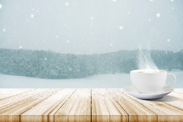 Cup of coffee on wooden table with winter snowfall covered forest. Christmas and New year background.