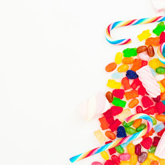 Assorted colorful bright candies and sugar cane on white background. Flat lay, top view