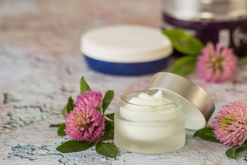 Obraz na płótnie Canvas Natural cosmetic. Small jars with cream to care for skin of face and body, next to fresh clover flowers on a light background.