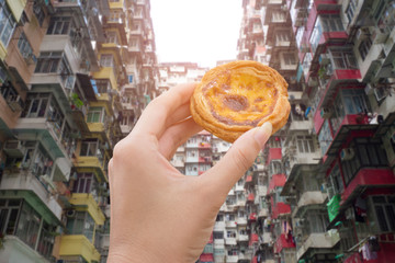 hand holding egg tart with old apartment in hongkong