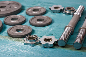 Close up of metallic weight plates on wooden floor and dumbbells in background