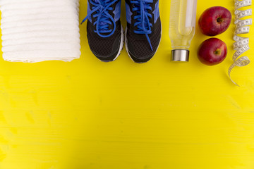Fitness equipment. Healthy food. Sneakers, water,apple, measuring tape on yellow wooden background