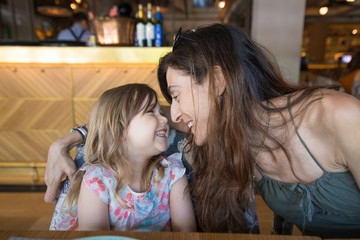 three years old blonde girl looking to woman mother laughing sitting in restaurant

