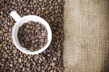 Fototapeta na wymiar roasted arabica coffee beans in coffee cup with sack cloth background.roasted coffee beans pattern