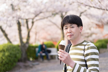 満開の桜の木の下でアイスクリームを食べる男性