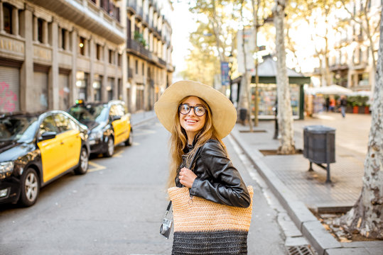 Woman tourist in hat crossing the street with yellow painted taxi traveling in Barcelona city