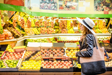 Woman standing in front of the food store showcase with fruits and vegetables