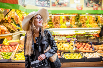 Woman standing in front of the food store showcase with fruits and vegetables