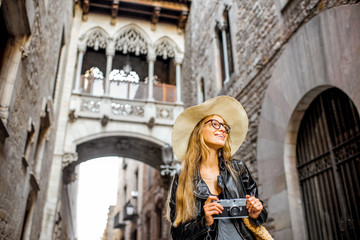 Naklejka premium Young woman tourist in hat standing with photo camera in front of the famous bridge of sighs in Barcelona old town
