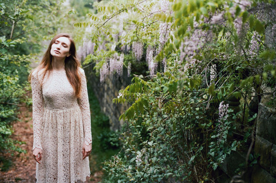 Beautiful young woman standing among wisteria