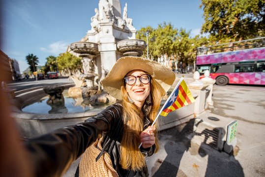 Young woman tourist making selfie photo with catalan flag near the fountain in Barcelona city