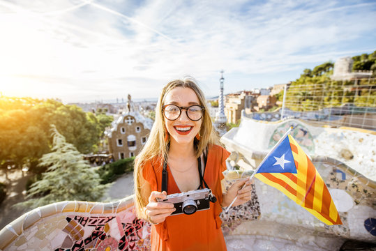 Portrait of a young woman tourist in red dress with catalan flag visiting famous Guell park in Barcelona