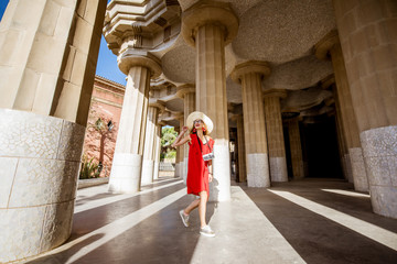 Naklejka premium Happy woman tourist in red dress with hat walking near the columns visiting famous Guell park in Barcelona