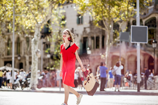 Lifestyle portrait of a beautiful woman in red dress crossing the central city avenue in Barcelona
