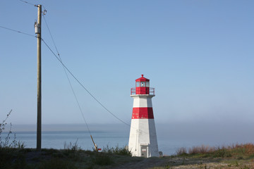 Small coastal unmanned lighthouse with bright red highlights beside the Power Line bringing it electricity.