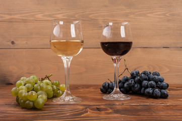 Red and white wine glasses and grape on wooden table