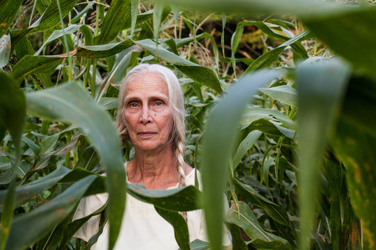 Elderly blonde woman with braids standing in corn field