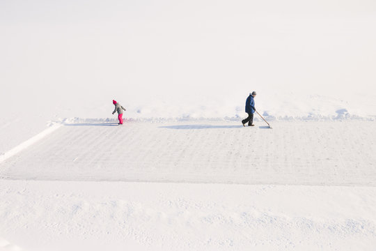 Father clears ice rink on lake while daughter skates