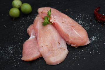 Raw Chicken fillet with spices on a black background.