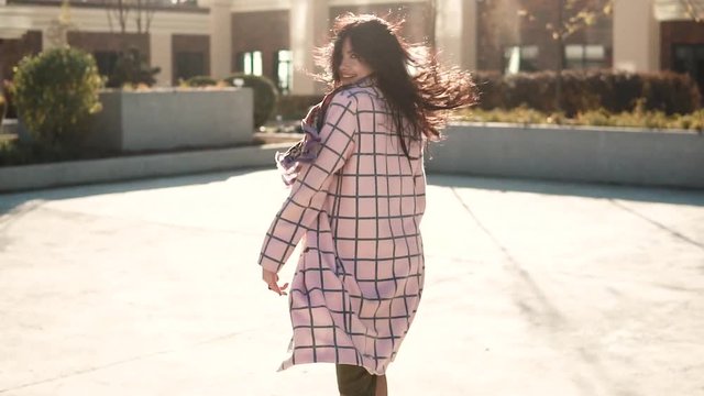 attractive young woman playfully turns around at the camera. girl in autumn coat with back view. the girl is running from the camera. slow motion